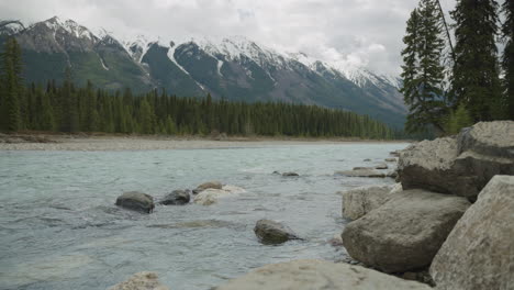 A-stream-with-snow-capped-mountains-in-the-background,-in-the-Canadian-Rocky-Mountains