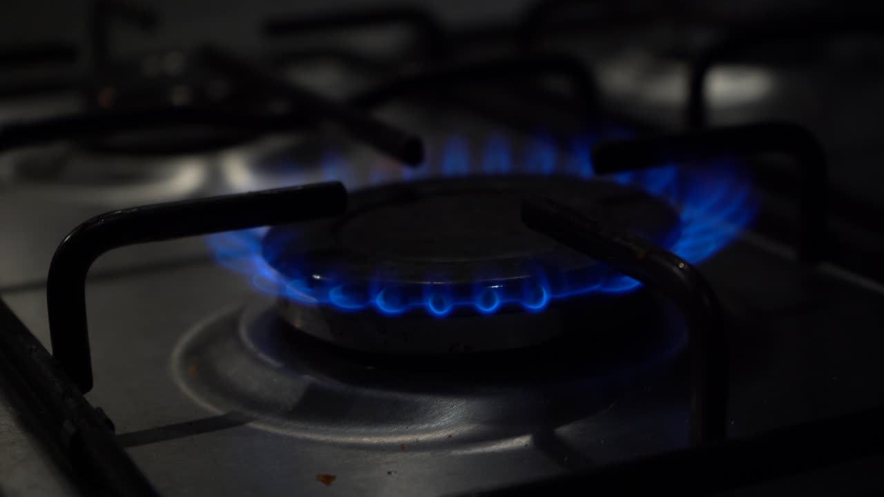 어두운 클로즈업:가스 스토브 버너에서 파란 불꽃이 점화된 다음 꺼집니다.