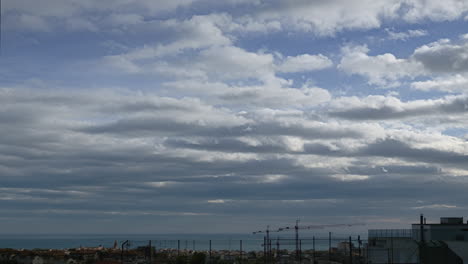 Wolken,-Die-Sich-Schnell-über-Den-Himmel-Bewegen,-überschatten-Die-Stadt-Am-Meer-Und-Schaffen-Bei-Düsterem-Wetter-Eine-Neblige,-Trübe-Atmosphäre-In-Der-Ferne-über-Der-Geschäftigen-Metropole