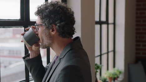 happy-mature-business-man-drinking-coffee-at-home-enjoying-relaxed-morning-looking-out-window-planning-ahead-thinking-successful-caucasian-male-smiling-wearing-glasses-in-apartment-loft