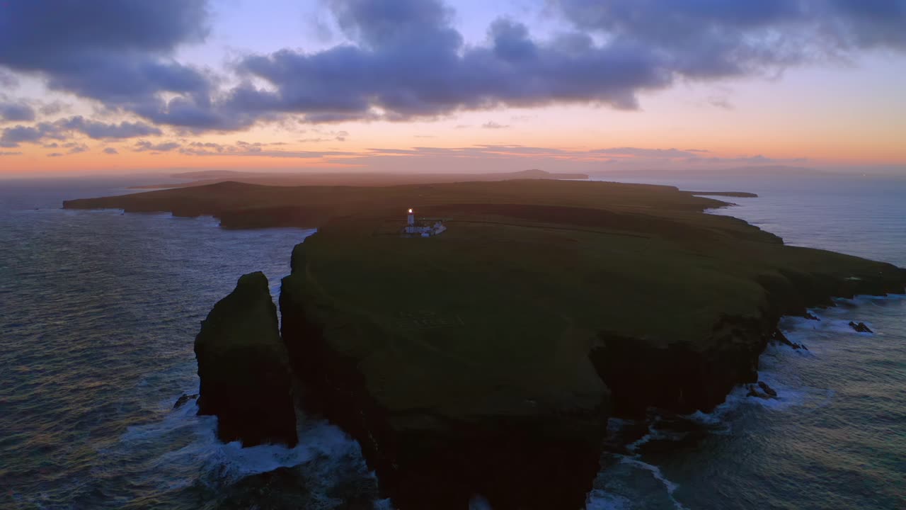 Pullback drone shot of Loop Head Peninsula at dawn with lighthouse beaming. Ireland.