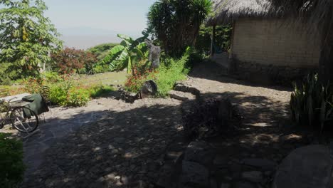 dolly-in view of rustic garden with flowers, trees, and thatched roof structure. superadobe earth bag round rustic kitchen
