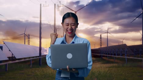asian female with her laptop with solar panel and wind turbines, she raises her fist up with screaming goal