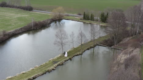 Frischvermähltes-Paar-Spaziert-Im-Herbst-Auf-Schmalem-Weg-Zwischen-Seen