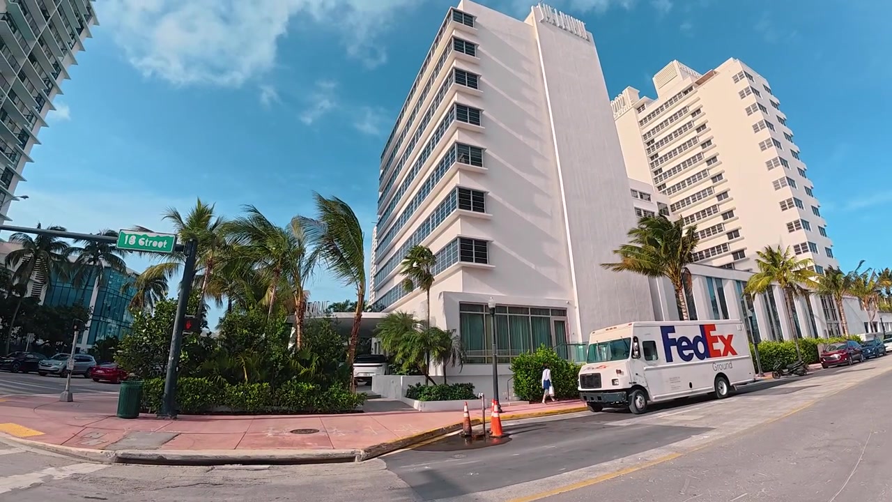 Miami, EUA, 16 de julho de 2026: Cruzamento de rua e edifícios em Miami Beach. Estrutura de hotel branca, placa de rua, furgão de entrega estacionado na estrada, torres residenciais altas, palmeiras, céu diurno.
