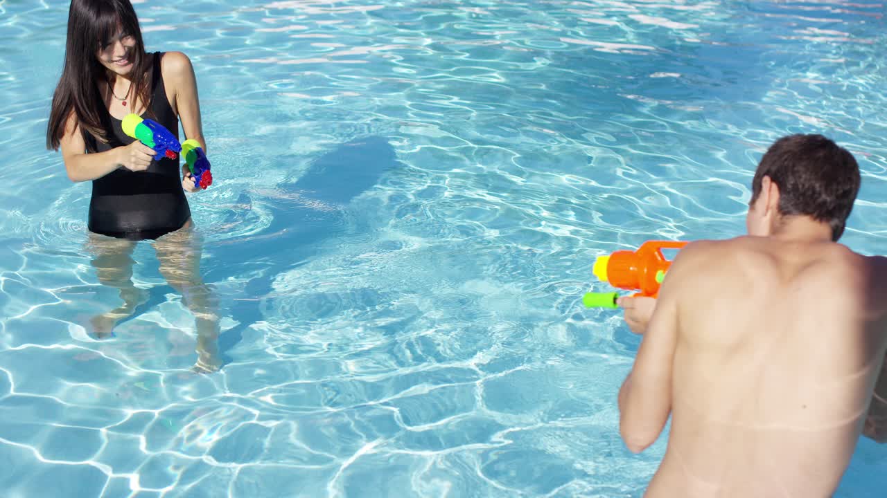 Casal fofo brincando com pistolas de água na piscina