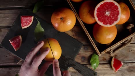 men's hands cut the grapefruit in two halves on the cutting board.