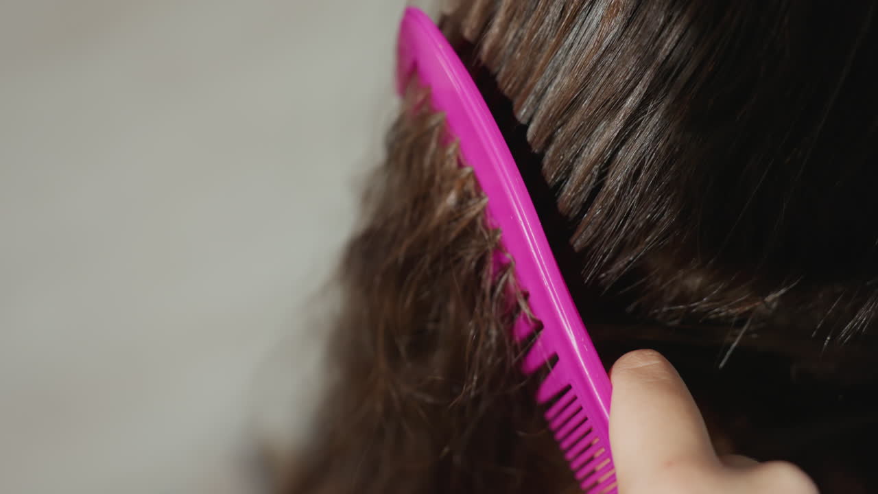 CloseUp Combing Tangled Hair Strands With Pink WideTooth Comb, AtHome Caregiver Gently Detangling Frizz And Knots, Soft Bathroom Light, Soothing Slow Motions, Focus On Texture And Strand Repair