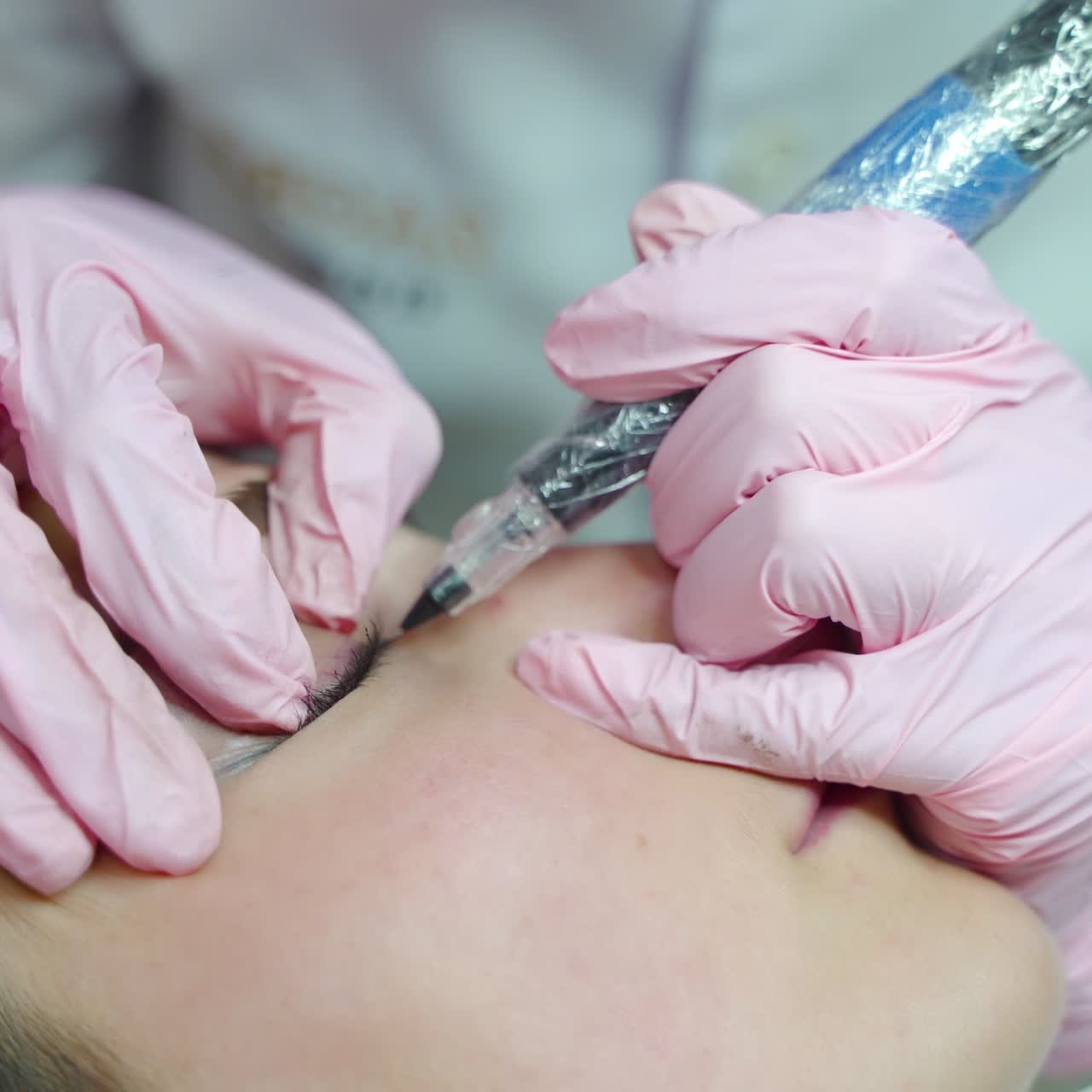 a beautician in gloves is making a permanent makeup of eye for a woman with the using of a professional needle. Modern cosmetology methods