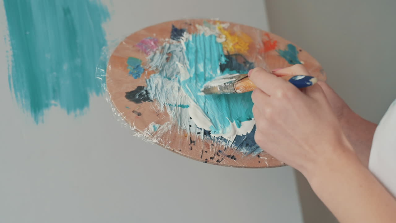 화가의 팔레트에서 색상을 혼합하는 인식할 수 없는 소녀의 손