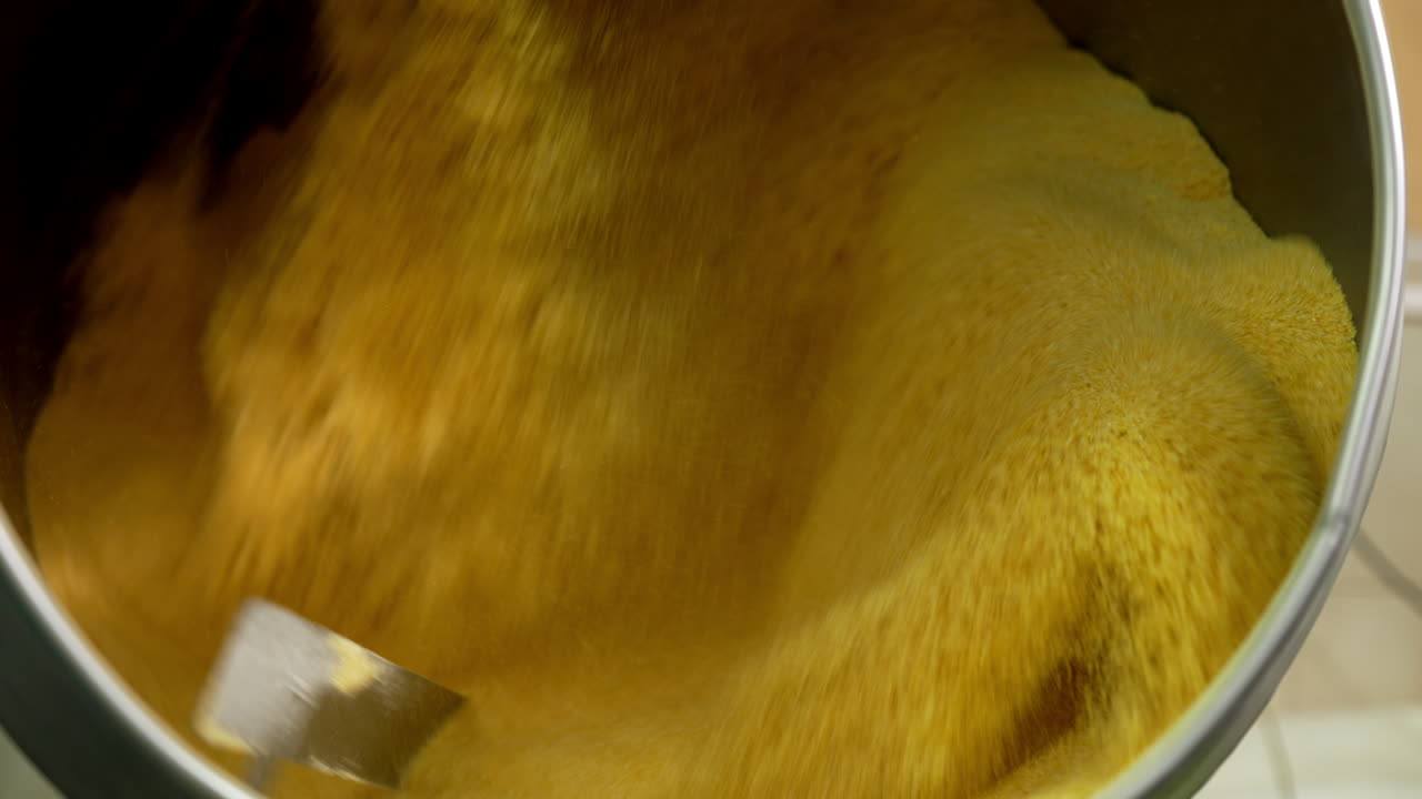 Yellow grinded corn being mixed in large rotating tank. Preparation of substance for sweet snacks manufacturing.