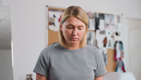 costumer focusing intensely while folding fabric, lifting head up with serious expression in creative workspace, surrounded by blurred background of colorful fabric samples and inspiration boards