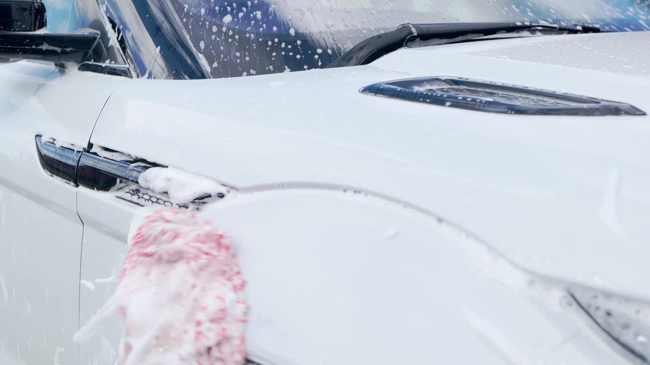 Close up cleaning white SUV with red microfibre wash mitt and lots of suds