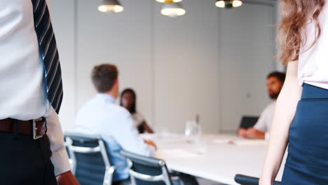 Close-Up-Of-Businessman-And-Businesswoman-Shaking-Hands-In-Modern-Boardroom-With-Colleagues-Meeting-Around-Table-In-Background-Shot-In-Slow-Motion