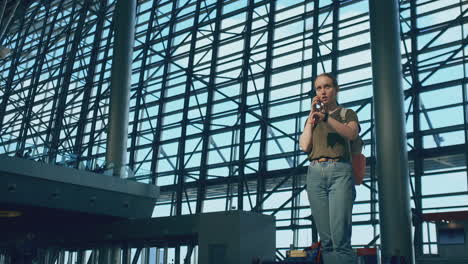 Standing-at-the-display-with-information-about-the-departure-of-aircraft-at-the-airport-a-young-girl-with-a-backpack-talking-on-a-mobile-phone