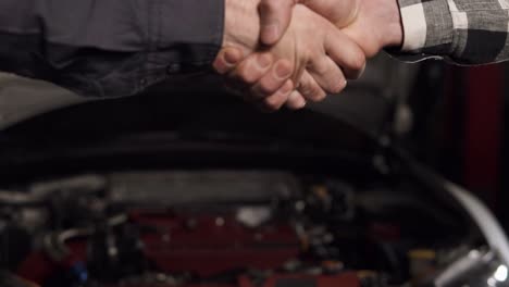 una foto de cerca del mecánico y el cliente estrechando la mano en un taller de reparación de automóviles.
