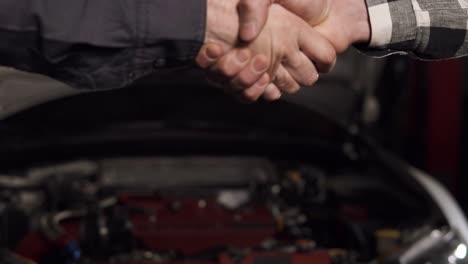 close up shot of mechanic and customer shaking hands in an auto repair shop.