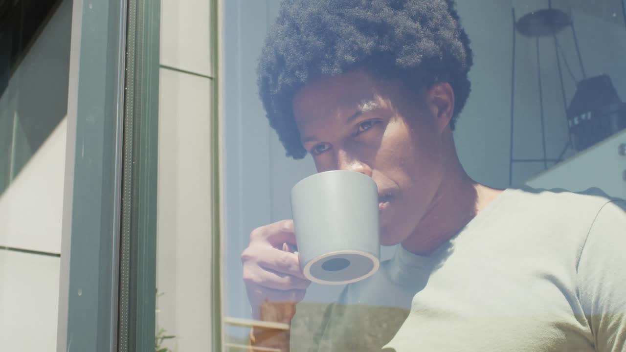 hombre afroamericano mirando por la ventana y bebiendo café en casa