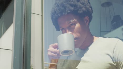 hombre afroamericano mirando por la ventana y bebiendo café en casa