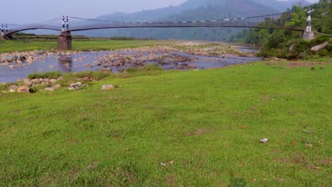 Puente-Colgante-De-Hierro-Aislado-Sobre-El-Río-Que-Fluye-Con-Fondo-De-Montaña-Y-Cielo-Azul-En-El-Video-De-La-Mañana-Se-Toma-En-Nongjrong-Meghalaya-India