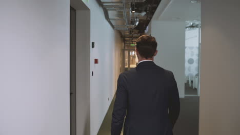 Following-an-unrecognizable-businessman-through-the-hallway-of-an-office-building