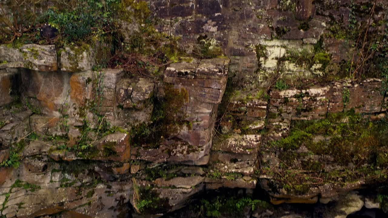 Aerial tilt up from water to walls of Aughnanure Castle, revealing medieval stone walls against white sky