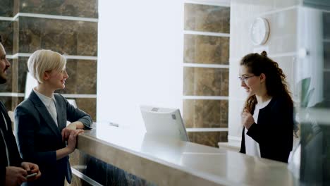 businessman and businesswoman guests come to receptionist girl and paying bill with credit card via contactless payment technology in hotel reception. business, travel and people concept