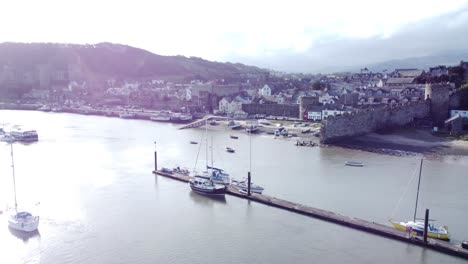 idyllic conwy castle and harbour fishing town boats on coastal shining waterfront aerial push in