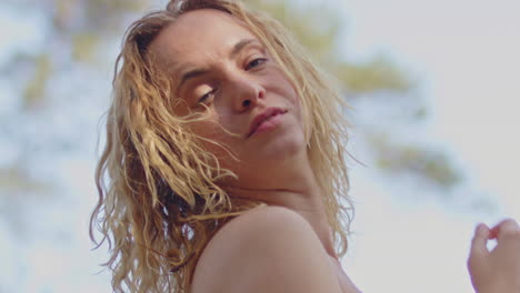 an attractive young woman stands outside in a sunny forest and looks down at the camera in slow motion