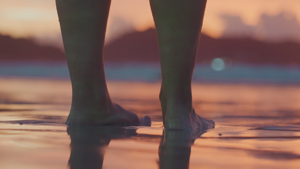 Donna di colore a piedi nudi sulla riva, con i piedi scoperti vicino all'acqua, avvolta dalla calma nella tranquilla luce della sera, mentre le dolci onde lambiscono la riva al tramonto.