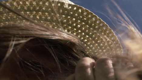 woman holding onto straw hat on windy day with hair blowing close up shot