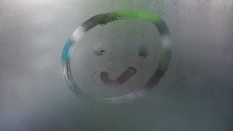 a finger draws a cheerful emoticon on a foggy window