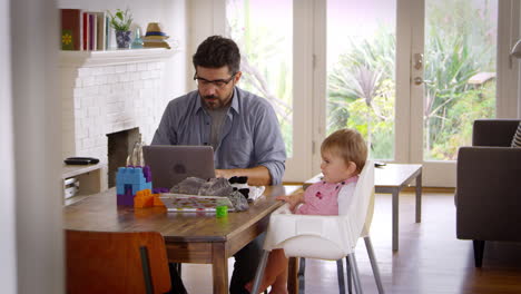 father working from home on laptop as son plays with toys