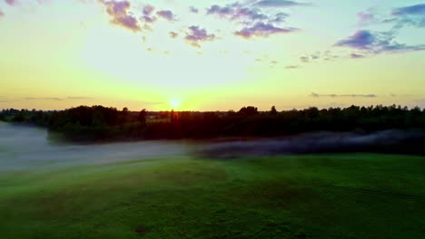 scenic rural landscape shrouded in fog and orange colored sunrise at horizon