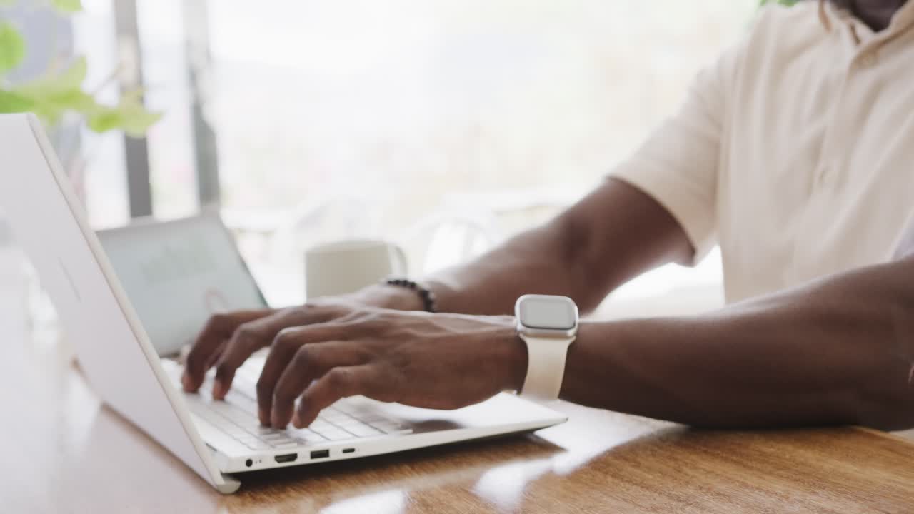 African American man starting work at table, typing on white laptop, wearing beads finishing task