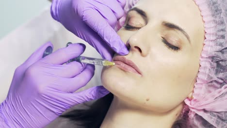 close up of the hands of cosmetologist in gloves doing injection to the lips of the woman in medical cap. lips procedure