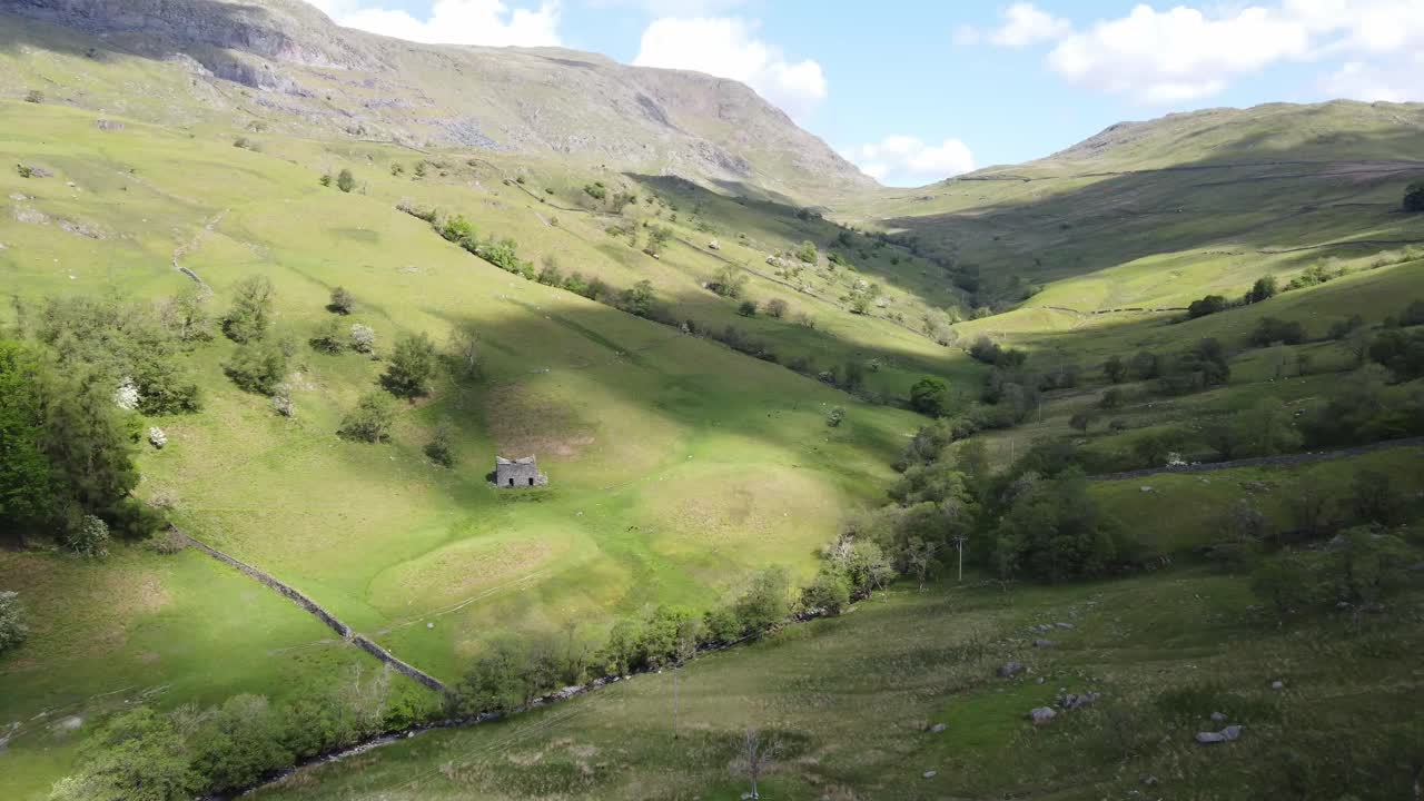 Veduta soleggiata con drone della valle di Kirkstone Pass con ombre di nuvole sui campi, guardando verso Red Screes Fell con un vecchio edificio agricolo