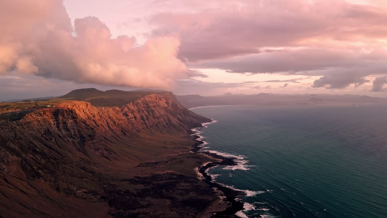 Stunning aerial drone footage of Famara Beach and its dramatic coastal mountains during golden sunset light in Lanzarote, Canary Islands, Spain.
