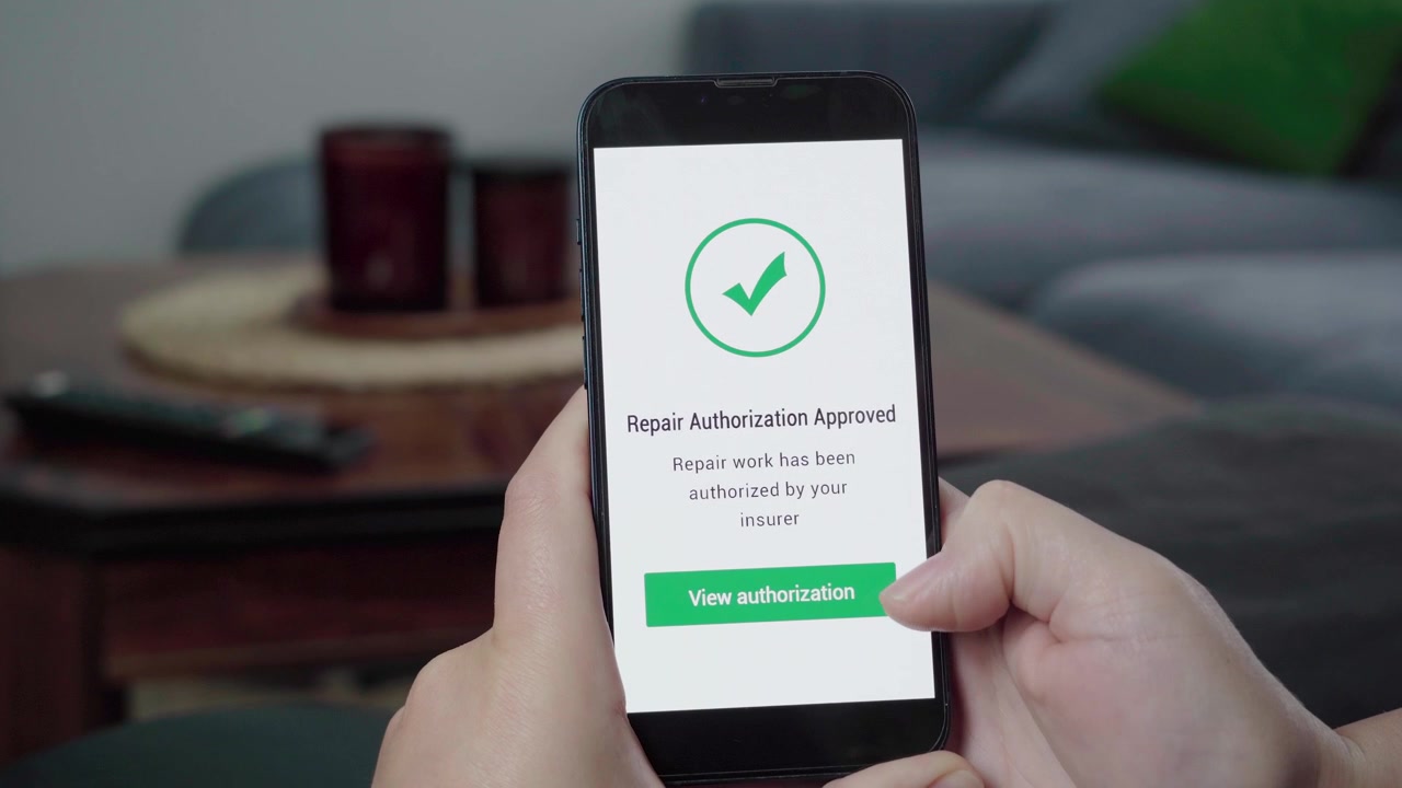 Una persona controlla un'app assicurativa che conferma l'autorizzazione alla riparazione con un segno di spunta verde di approvazione sullo schermo.