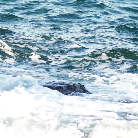 natural view of waves breaking into dark rocks near beach. sea waves with white foam on the dangerous stones. ocean waves crashing against the rocks on the shore. close-up.