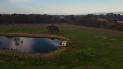 órbita-Aérea-Disparada-Sobre-Una-Casa-Pequeña-Y-Un-Lago-Espejo-Durante-Una-Puesta-De-Sol-Nublada