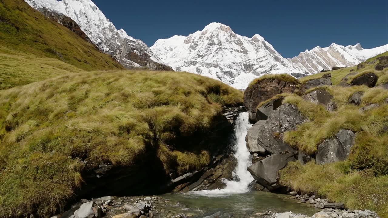 Waterfall Stream and Himalayas Landscape in the Mountains in Nepal, Snowy Snowcapped Big Mountain Summit and Flowing River Scenery in High Altitude Terrain at Annapurna Base Camp