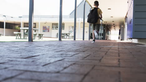 Biracial-boy-with-a-backpack-walks-away-in-a-school-corridor-with-copy-space