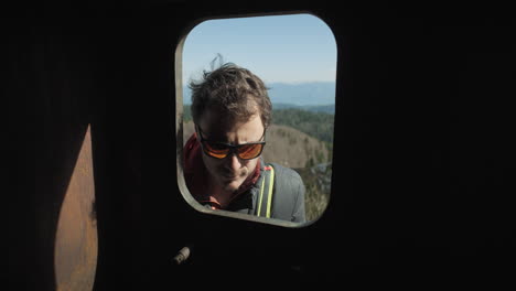 a hiker with a green backpack stopping at the window to look inside and than continuing his jurney