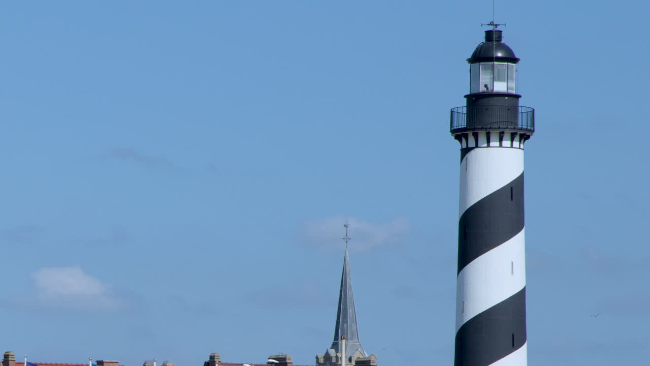 Camera pans from striped lighthouse to colorful rooftops and beach promenade under bright daylight