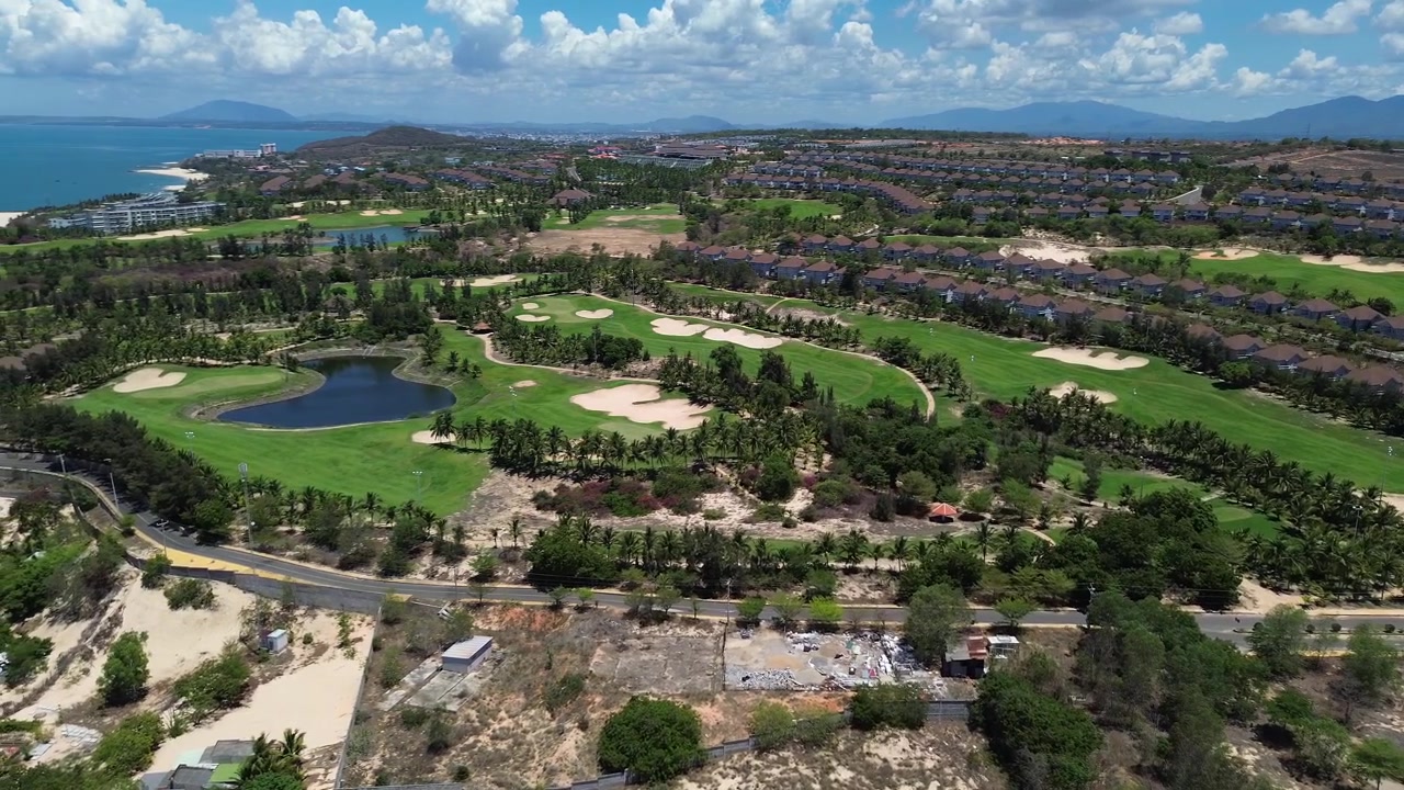 Riprese aeree con drone che mostrano fairway da golf verdi e aree di gioco curate a Mui Ne, Phan Thiet, Vietnam, circondate da vegetazione tropicale e situate vicino al litorale costiero