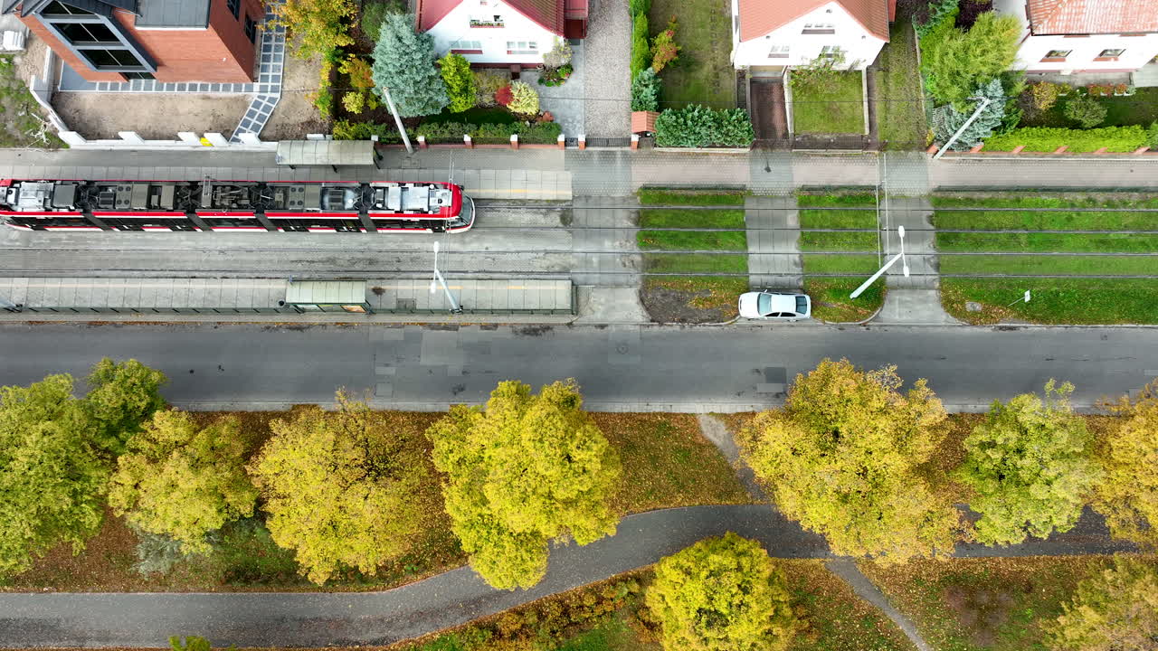 Drone view of tram passing residential area surrounded by colorful autumn trees