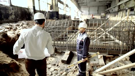 ingenieros profesionales que trabajan juntos en el sitio de construcción. arquitecto jefe caminando hacia el trabajador de pie cerca del encofrado de la fundación. constructor con nivel escuchando al capataz esperando instrucciones