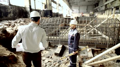 professional engineers working together on construction site. chief architect walking to worker standing near formwork of foundation. builder with level listening to foreman waiting for instructions