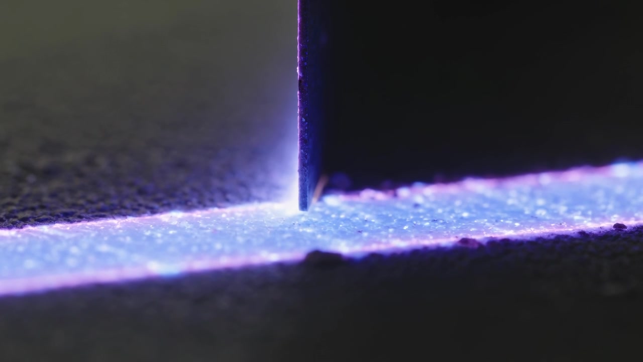 Sænker en tynd metalklinge, der rører et smalt violet glødende bånd på en mørk overflade, og viser en glorie.